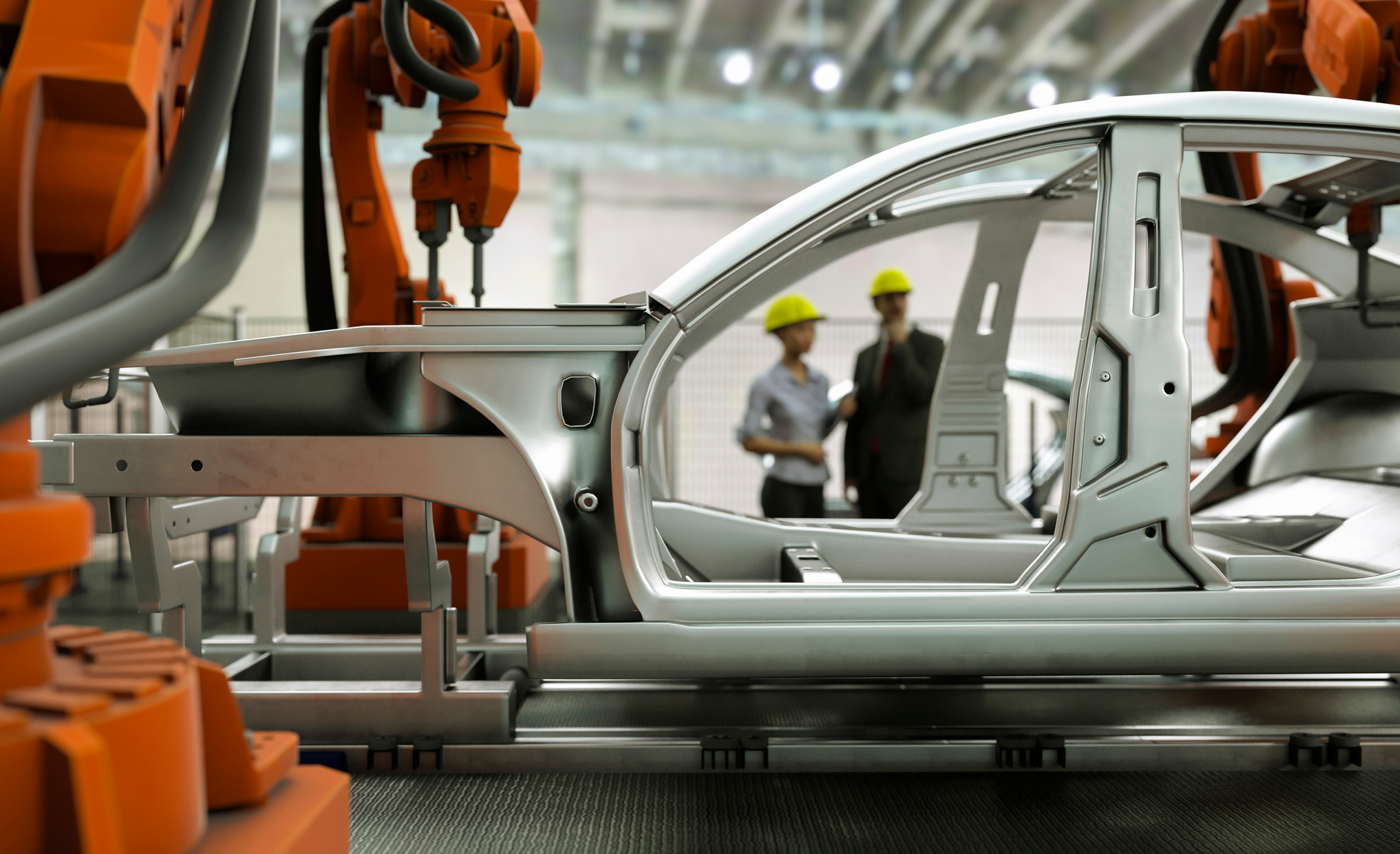 orange robot arms welding a silver car frame on an assembly line